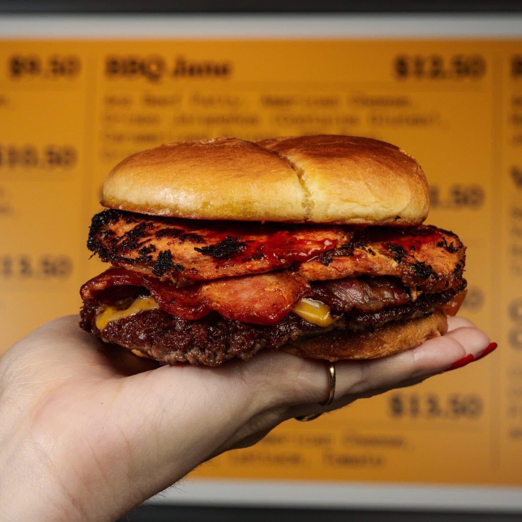 A person holding Harry's Charbroiled burger in front of Harry's yellow menu.